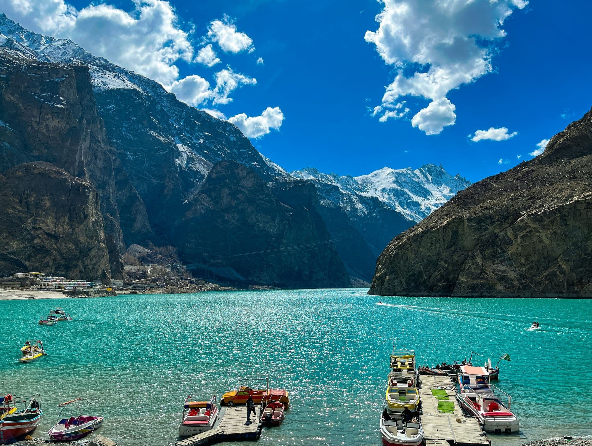 Wooden boats moored on the turquoise water of Attabad Lake, Hunza, with bare brown mountains rising behind