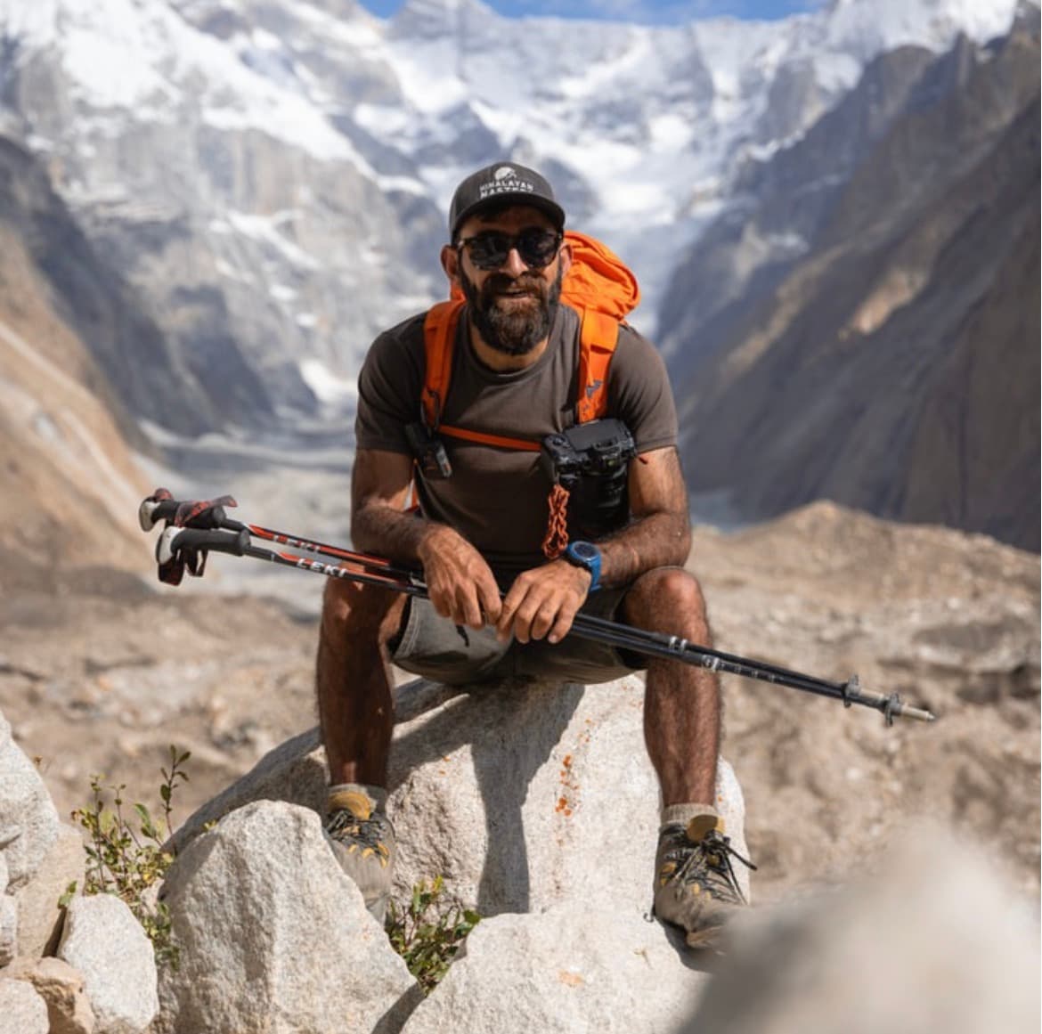 Sohail Sakhi resting on a boulder with trekking poles below a snow-covered Karakoram peak